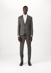 Costume pour homme gris en tissu lisse, avec une veste à un bouton, des revers en pointe et un pantalon slim-fit. Chemise blanche en dessous avec des boutons noirs.