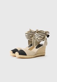 Spissespissede espadriller med en beige og svart fargepalett, som har stripete stoffbue-detaljer og vevde jute-såler. Åpne sider og rund tå.