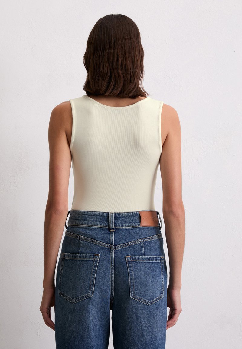 Biały prążkowany podkoszulek z okrągłym dekoltem, noszony z niebieskimi dżinsami z wysokim stanem, które mają brązową skórzaną metkę marki i detale kieszeni.