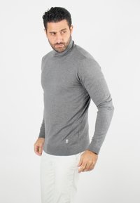 Pull à col roulé gris avec des manches longues, des poignets et un ourlet côtelés, fabriqué en matière tricotée douce, avec un petit logo en bas.