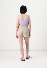 Débardeur côtelé violet clair associé à un short beige texturé avec une taille élastique, vu de dos, porté avec des sandales plates.