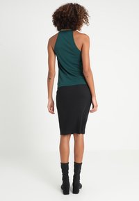 Grön ärmlös topp med hög halsringning, tillsammans med en svart ribbad kjol, bärs med knähöga svarta klackstövlar. Släta texturer, figursydd design.