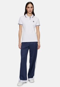 Weißes Poloshirt mit Kragen und mehrfarbigen Streifenakzenten. Navygestreifte Hose mit weißen Seitendetails und weißen Sneakers.