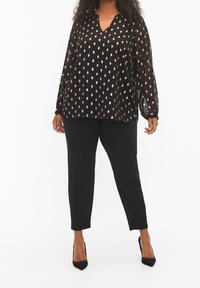 Blusa nera con pois rosa, design a V, maniche lunghe e tessuto leggero. Abbinata a pantaloni neri slim-fit e tacchi.