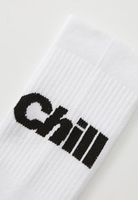 Valged ribakotid, millel on esikohal sõna "Chill" mustas tekstis. Materjal tundub pehme ja sileda tekstuuriga.