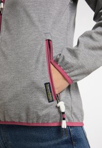 Giacca grigia con zip e dettagli rosa, dotata di tasca laterale, polsini elastici e un cordoncino con dettagli bianchi e rosa.