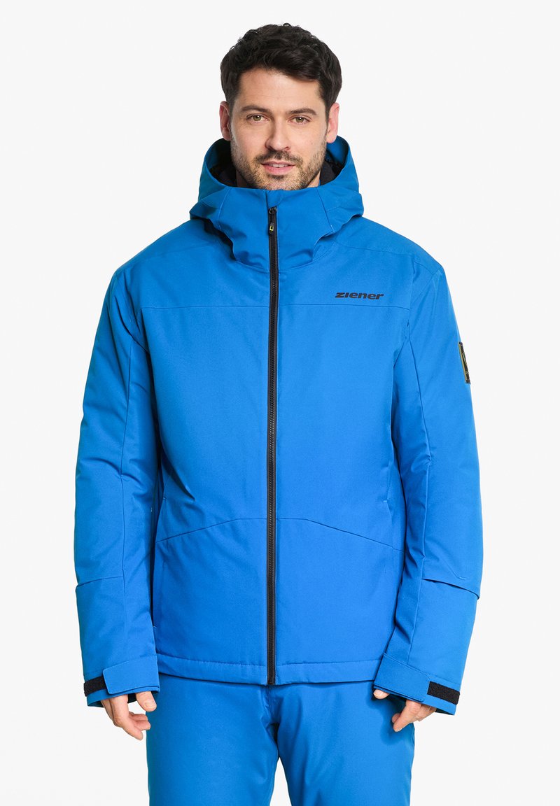 Giacca isolante blu con cappuccio, dotata di una cerniera frontale, polsini regolabili e un logo sul petto. Texture liscia, vestibilità su misura.