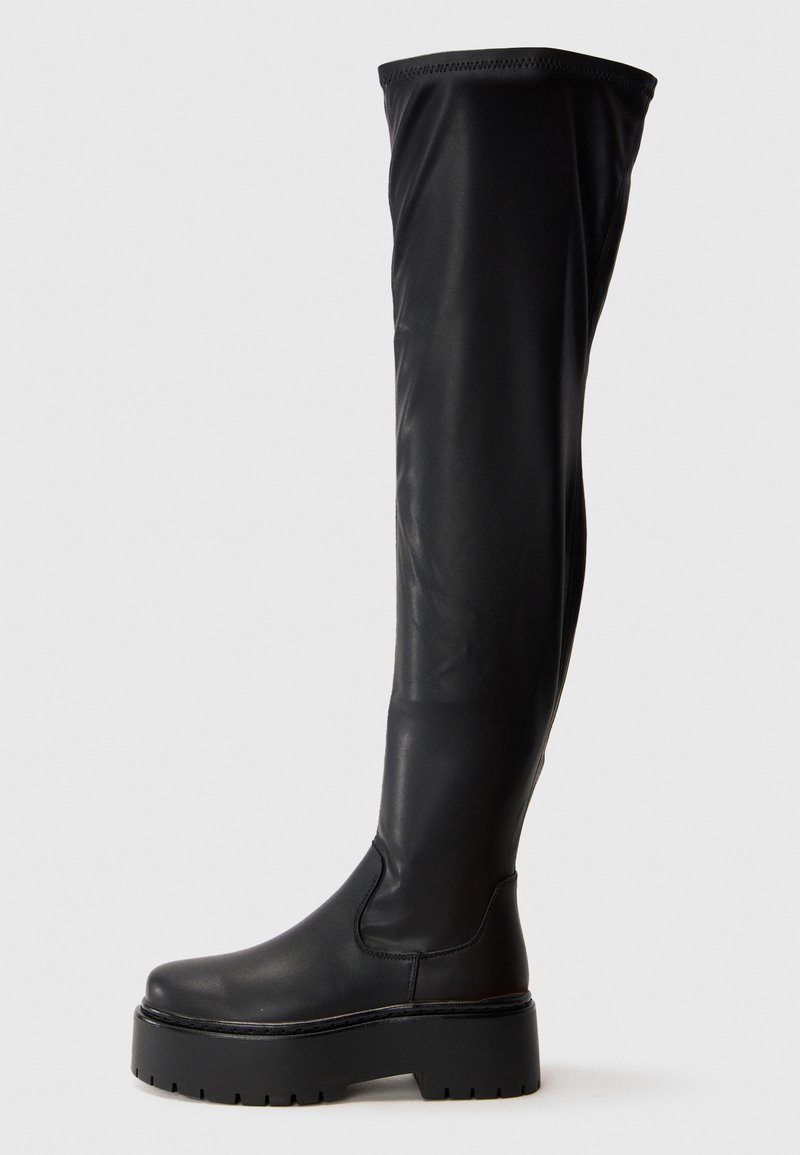 Sorte over-the-knee støvler laget av glatt syntetisk materiale. Har en rund tå og chunky plattformsåle med teksturert såle.