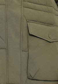 Maslinasto zelena puffer jakna s kvadratnim teksturom, koja ima preklopnu džep sa dugmetom na rasporu i vidljivim šavovima.