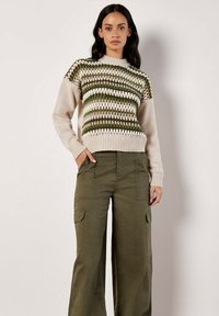 Sweter z dzianiny w kolorze kremowym z zielonymi i brązowymi pasami, z okrągłym dekoltem i ściągaczami przy mankietach, w połączeniu z oliwkowymi spodniami cargo.