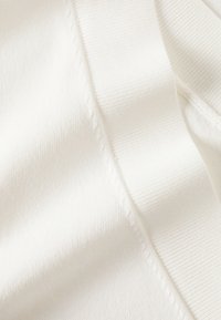 Tessuto bianco con una superficie liscia e una leggera lucentezza. Include una sezione a coste e cuciture piatte lungo i bordi.