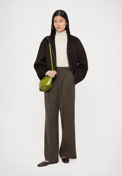 Jachetă maro cu fermoar, pulover crem cu guler înalt, pantaloni evazați verde măsliniu și poșetă transversală verde. Pantofii de culoare roșu închis finalizează ținuta.