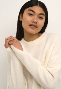 Kremowy, oversize'owy sweter wykonany z miękkiego materiału, z szerokim dekoltem i prążkowanymi akcentami na rękawach oraz na dolnym obszyciu.