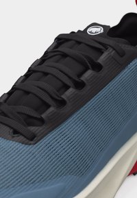 Nahaufnahme eines blauen und schwarzen Sneakers mit gerippter Textur, schwarzen Schnürsenkeln und einem weißen Logo auf der Zunge.