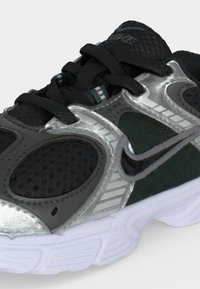 Μαύρο και ασημένιο παπούτσι για τρέξιμο Nike με μαύρα κορδόνια, δίχτυ και λευκή υφή στη σόλα.