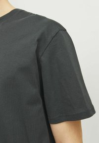 Camiseta de algodón en color gris carbón con escote redondo, mangas cortas y una textura suave. Diseño simple sin patrones ni detalles visibles.