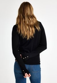 Zwarte trui met lange mouwen, voorzien van gouden knoopaccenten bij de manchetten. Het materiaal lijkt glad, met een aansluitend ontwerp en een geribde zoom.