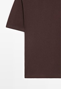 T-shirt à manches courtes de couleur brun foncé, montrant le haut du torse et le bord de la manche sur un fond blanc.