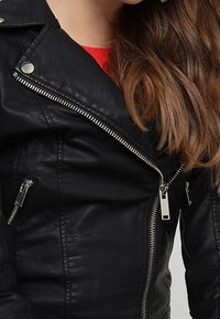 Giacca in ecopelle nera con zip diagonale, accessori in argento e multiple tasche con zip. Texture liscia e design aderente.