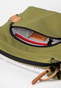 Grüne Nylon-Tasche mit Reißverschluss, ausgestattet mit einem Lederelement und einem gemusterten Innenfutter. Enthält eine rote Innentasche und ein Karomuster-Futter.