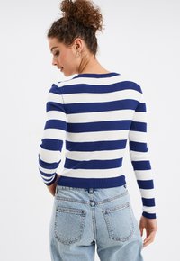 Blau-weißer gestreifter Rippstrickpullover mit langen Ärmeln und rundem Halsausschnitt, kombiniert mit hellblauen hochgeschnittenen Jeans.