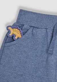 Blaue Jogginghose mit einer strukturierten Oberfläche. Ein gelbes Dinosaurier-Patch mit braunen Akzenten ist in der Fronttasche sichtbar. Verstellbarer Kordelzug.