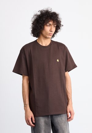 Brown cotton t-shirt with a relaxed fit, short sleeves, crew neckline, and small gold logo on the chest. Simple design and solid color.