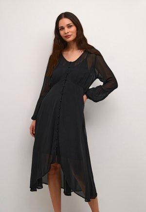 Black long-sleeve dress made of sheer fabric, featuring a buttoned front, gathered waist, and an asymmetric hemline. Smooth texture.