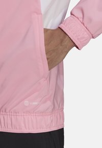 Helles rosa Jacket mit elastischen Bündchen und Saum, verfügt über eine Seitentasche. Der Stoff ist glatt und wasserabweisend, mit dem Branding "Aeroready."