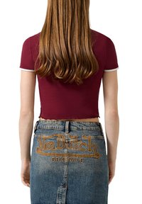 Bordeaux cropped t-shirt met korte mouwen en witte biezen, gecombineerd met een high-waisted blauwe denim rok met een bruin geborduurd logo.