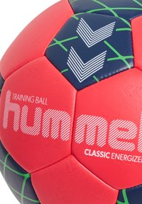 Pallone da allenamento rosso e blu realizzato in materiale sintetico. Presenta accenti geometrici verdi e una superficie texturizzata. Il logo del marchio è mostrato in modo prominente.