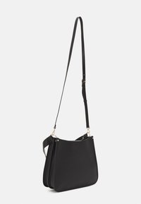 Svart axelväska med en slät yta, utrustad med en smal justerbar rem och guldiga metallaccenter. Tredimensionell profil, minimalistisk design.