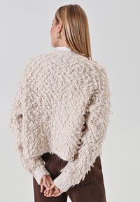 Pull crème texturé avec matière bouclée, coupe courte, poignets côtelés et coupe décontractée. La vue de face n'est pas visible sur l'image.