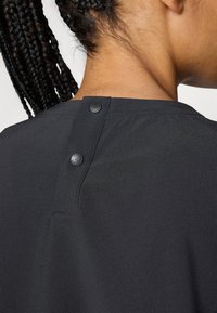 Prenda negra con una textura suave, con un escote redondo, dos botones negros en la parte posterior y un sutil detalle de costura.