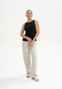 Schwarzes geripptes Tanktop, hellbeige weite Hose und helle Sandalen. Glatte Stoffe, figurbetontes Oberteil, lässiges Gesamtdesign.