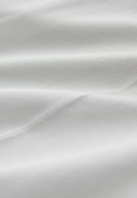 Tissu blanc doux avec une fine texture diagonale en sergé et des plis légers créant des ombres et des reflets subtils.