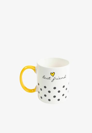 Tazza di ceramica bianca con pois neri, cuore giallo e manico; presenta il testo "migliore amico" in carattere corsivo nero.