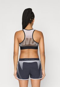 Top desportivo preto com parte traseira em rede e gráfico proeminente. Combinado com calções escuros exibindo padrão em rede e detalhes brancos.