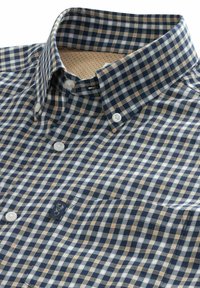 Camisa de hombre con botones y patrón de cuadros en azul marino, blanco y beige. Presenta un cuello clásico y un pequeño logo en el bolsillo del pecho.