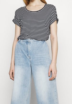 Camiseta de rayas blancas y negras con mangas enrolladas, combinada con jeans de pierna ancha en azul claro. El material parece suave y tiene un corte relajado.