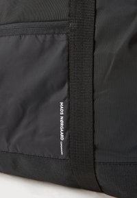 Približan prikaz crne platnene torbe sa zatvaračem i vertikalnom trakicom, koja sadrži bijeli logo s tekstom "MADS NØRGAARD COPENHAGEN".