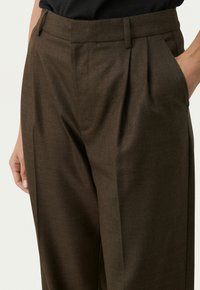 Bruine op maat gemaakte broek met een gladde textuur, geplooide voorkant en zijzakken, en een aansluitende tailleband voor een gestructureerde silhouet.