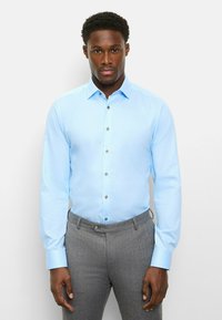 Hellblaues Hemd mit Knöpfen und langen Ärmeln, graue strukturierte Hose und kontrastierende Knöpfe. Glatter Stoff mit maßgeschneiderter Passform.