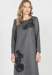 Szara sukienka z długimi rękawami, ozdobiona teksturowanymi czarnymi kwiatami z tkaniny ułożonymi asymetrycznie na piersi i na dolnej stronie. Gładkie wykończenie tkaniny.
