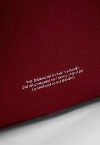 Povrch zůpavé látky s bílým vícejazyčným textem uvádějícím "Značka se 3 pruhy" v angličtině, němčině a francouzštině.