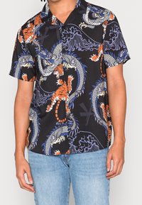 Czarna koszula z krótkim rękawem z żywymi wzorami smoka i tygrysa w kolorach pomarańczowym, niebieskim i białym. Gładka tkanina, luźny krój, zapinana na guziki.