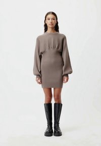 Ribbenbraunes Strickkleid mit langen Ballonärmeln und taillierter Silhouette, kombiniert mit kniehohen schwarzen Lederstiefeln.