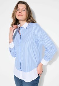 Camisa de botones de rayas azul claro y blanca, con mangas largas y puños blancos en contraste; presenta un dobladillo curvado y un cuello.