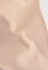 Hladká béžová látka s jemným šitím pozdĺž okraja, ukazujúca textúru a mierne zakrivené záhyby.