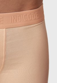 Beige stretch-stoff boksershorts med en myk elastisk midjebånd som har det pregete logoet "INDICODE." Sømdetaljer langs sidene.